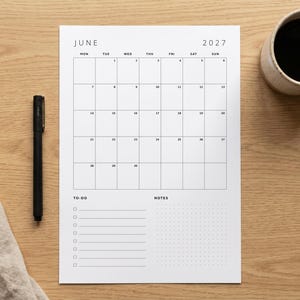 May include: A white paper monthly calendar for June 2027 with a black grid layout. The calendar includes a section for to-do lists with checkboxes and a dotted notes section. A black pen is positioned to the left of the calendar page.