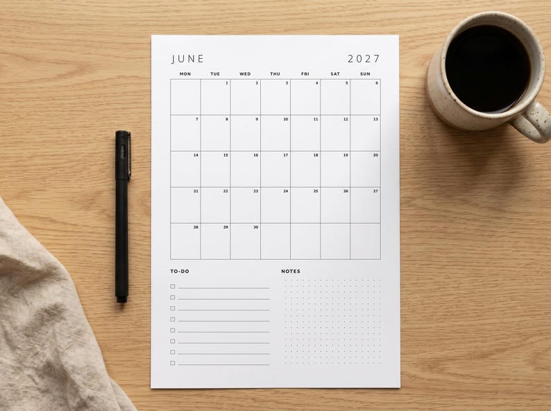 May include: A white paper monthly calendar for June 2027 with a black grid layout. The calendar includes a section for to-do lists with checkboxes and a dotted notes section. A black pen is positioned to the left of the calendar page.