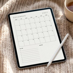 May include: A digital tablet displaying a December 2027 calendar page with a grid layout, a to-do list section with checkboxes, and a notes section. A white stylus rests on the screen, which features a clean, minimalist design with black text.