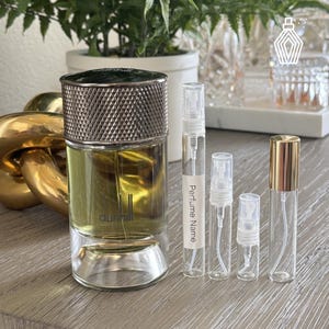 May include: A perfume bottle with a silver cap and a clear glass body, next to several small glass vials. The perfume bottle has a light green liquid inside. The vials are labeled "Perfume Name".