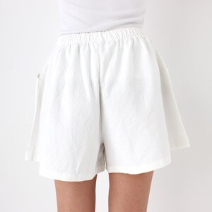 May include: White linen shorts with an elastic waistband. The shorts have a relaxed fit and pockets. The fabric appears to be lightweight and suitable for warm weather. The shorts are shown against a white background.