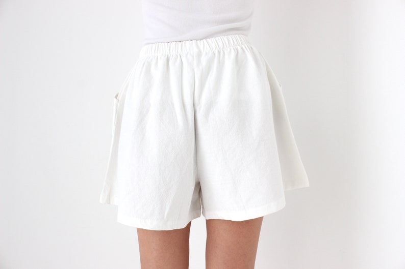 May include: White linen shorts with an elastic waistband. The shorts have a relaxed fit and pockets. The fabric appears to be lightweight and suitable for warm weather. The shorts are shown against a white background.