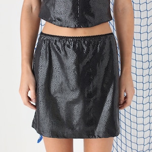 Puede incluir: Una minifalda negra con estampado de piel de serpiente. La falda tiene una cintura elástica negra.