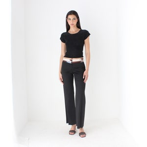 May include: A woman wearing a black short-sleeved shirt and black wide-leg pants with a patterned belt.
