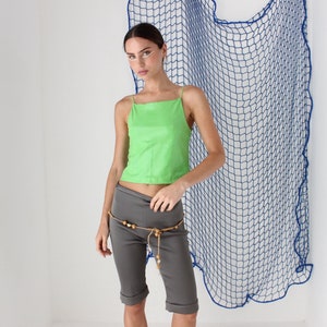 May include: A woman wearing a green tank top and gray shorts with a beaded belt. She is standing in front of a blue net.