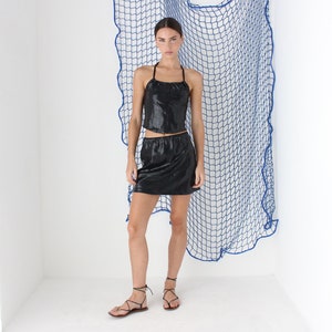 May include: A woman wearing a black sequined halter top and matching mini skirt. She is standing in front of a blue net backdrop.
