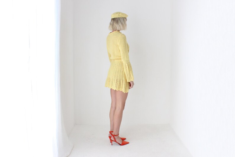 May include: A yellow crochet mini dress with bell sleeves and a matching beret. The dress is worn by a person with blonde hair and red heels.