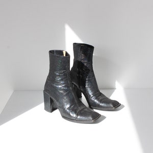 May include: A pair of black ankle boots with a chunky heel and a square toe. The boots have a glittery finish.