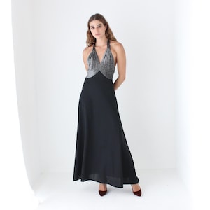 May include: A full-length black halter dress with a silver sequined bodice. The dress has a flowing skirt and is paired with burgundy heels. The model is standing in front of a white background.