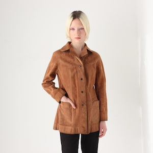 May include: A brown suede jacket with a collared neckline, button-down front, and two front pockets. The jacket is knee-length and has long sleeves. The model is wearing black pants.