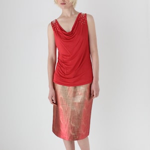 Puede incluir: Una blusa roja sin mangas con cuello de pico y una falda metálica dorada.