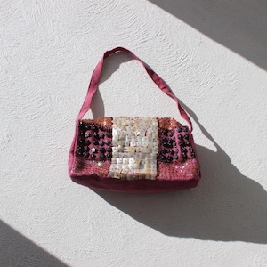 May include: A pink and white beaded handbag with a short strap. The bag is decorated with small, iridescent beads and has a rectangular shape.