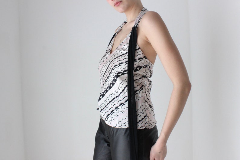 May include: A white halter top with a black and white abstract print. The top has a long black tie that hangs down the front.