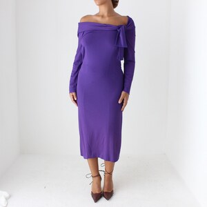 May include: A purple off-the-shoulder midi dress with long sleeves and a knot detail at the neckline.