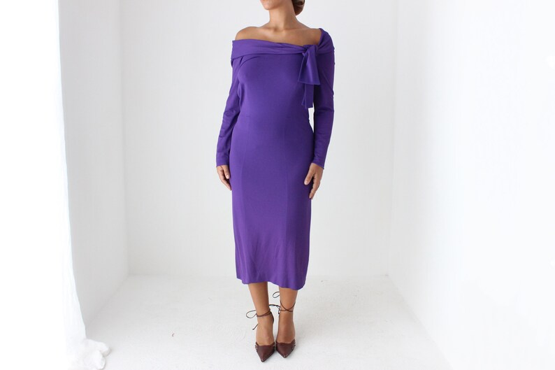 May include: A purple off-the-shoulder midi dress with long sleeves and a knot detail at the neckline.