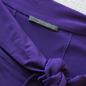 May include: A purple dress with a tie at the neck and a label that reads "Alberta Ferretti".
