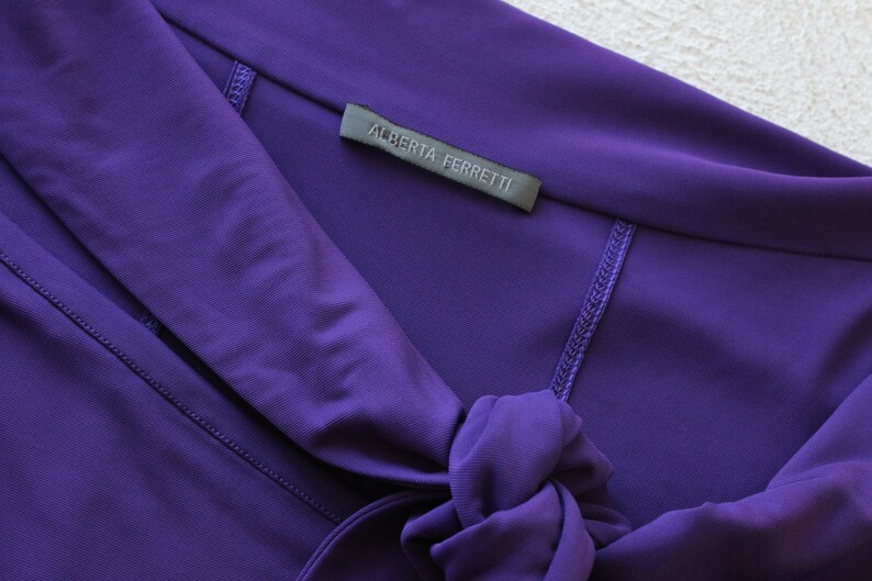 May include: A purple dress with a tie at the neck and a label that reads "Alberta Ferretti".