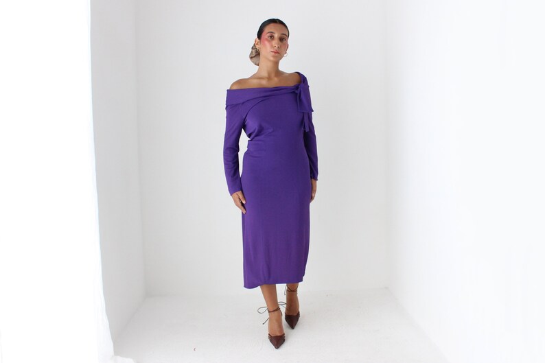 May include: A purple off-the-shoulder dress with long sleeves and a bow detail at the neckline.