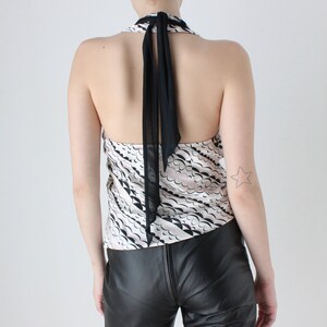 May include: A black and white halter top with a black sheer ribbon tie at the back. The top has a wavy pattern and is made of a silky fabric.