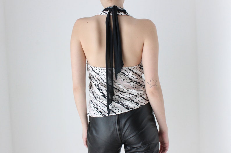 May include: A black and white halter top with a black sheer ribbon tie at the back. The top has a wavy pattern and is made of a silky fabric.