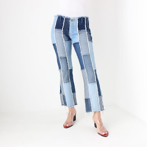 May include: A pair of blue denim jeans with a patchwork design. The jeans are made of different shades of blue denim and have a frayed hem.
