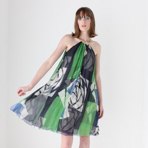 May include: A woman wearing a green, blue and white patterned halter dress with a gold chain detail.