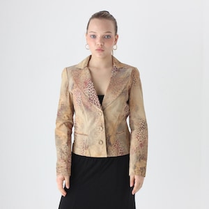 Op de afbeelding: Een beige blazer met een luipaardprint op de revers en mouwen. De blazer heeft een sluiting met twee knopen en een klassieke kraag. Het model draagt een zwarte rok.