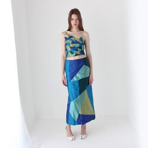 Può includere: Un completo a due pezzi composto da un top corto senza spalline monospalla e una gonna lunga e dritta. Entrambi i capi presentano un design patchwork geometrico nei toni del blu, verde acqua e verde lime con una lucentezza visibile.