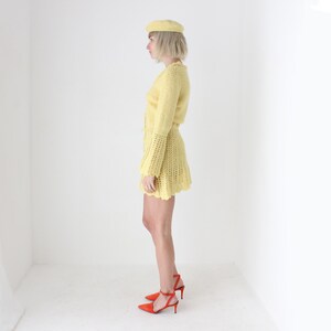 May include: A yellow crocheted dress with a matching beret. The dress has a fitted bodice and a flared skirt. The model is wearing red heels.