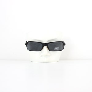 May include: Black rectangular sunglasses with a black frame and dark grey lenses. The sunglasses are on a white mannequin head.