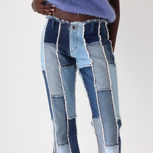 May include: A pair of blue denim jeans made from different shades of blue denim, sewn together in a patchwork style. The jeans have a straight leg and a raw hem.