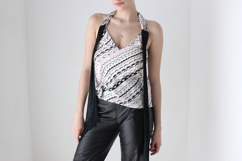 May include: A white halter top with a black and white wave pattern and black straps. The top is tied at the neck and has a deep V-neckline.