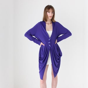 May include: A long-sleeved purple cardigan with a draped design and button closures. The cardigan is made of a soft, flowing fabric.