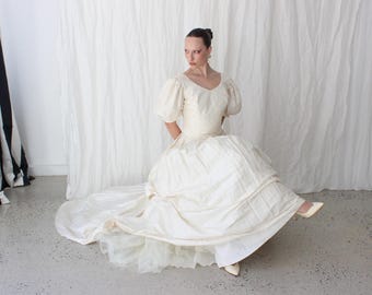 Magnífico vestido de novia vintage de los años 80 de seda cruda dupión color crema con mangas abullonadas, cintura vasca, corpiño con cuentas y cola.