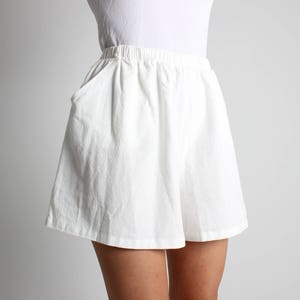 May include: White shorts with an elastic waistband and pockets. The shorts are made of a textured fabric and have a relaxed fit. The shorts are knee-length and suitable for casual wear.