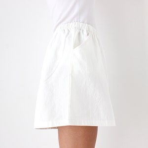May include: White skirt with an elastic waistband and a pocket. The skirt is made of a textured fabric and is knee-length. The model is wearing a white t-shirt.