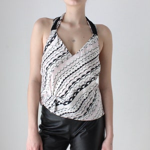 May include: A white halter top with a black and pink abstract pattern. The top has a V-neckline and a tie closure at the back.