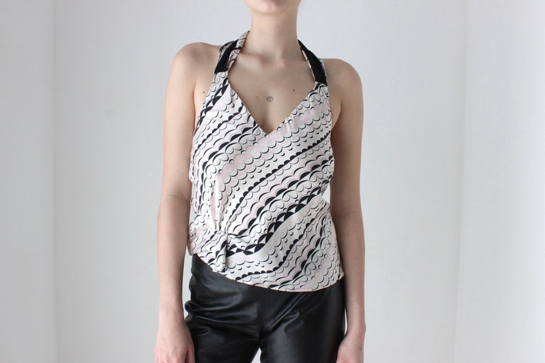 May include: A white halter top with a black and pink abstract pattern. The top has a V-neckline and a tie closure at the back.