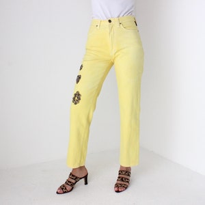 May include: A pair of yellow high-waisted jeans with leopard print embellishments. The jeans are straight-legged and have a relaxed fit.