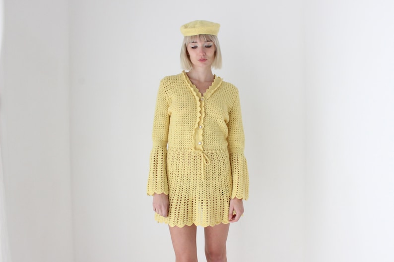 May include: A yellow crochet dress with bell sleeves and a crocheted hat.