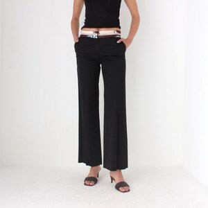 May include: Black wide-leg pants with a brown belt and a patterned fabric insert. The pants are worn by a person with bare arms and feet.