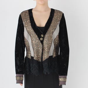 May include: Black velvet jacket with a V-neck, featuring gold sequin and grey panels. The jacket has long sleeves with gold trim at the cuffs and two gold buttons. The bottom of the jacket has a black lace trim.