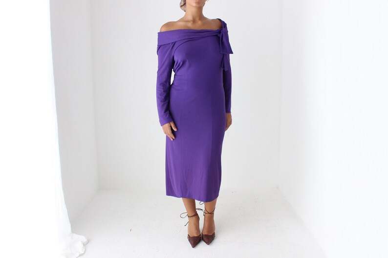 May include: A long-sleeved, purple off-the-shoulder dress with a bow detail at the neckline.
