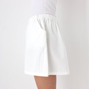 May include: White shorts with an elastic waistband and a side pocket. The shorts are made of a lightweight fabric and appear to be slightly textured. The garment is part of a casual clothing collection.