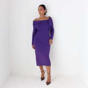 May include: A long-sleeved, purple dress with an off-the-shoulder neckline and a bow detail at the neckline.