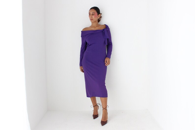 May include: A long-sleeved, purple dress with an off-the-shoulder neckline and a bow detail at the neckline.