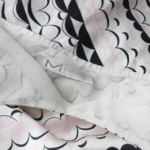 May include: White fabric with a black and pink cloud pattern. The fabric has a label that says "M by MADONNA".