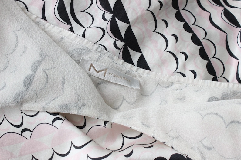 May include: White fabric with a black and pink cloud pattern. The fabric has a label that says "M by MADONNA".