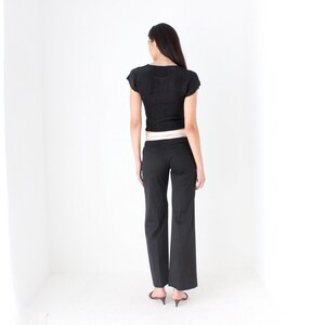 May include: A black cropped top with short sleeves and a black pair of pants. The pants have a wide leg and a light brown belt.