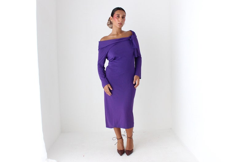 May include: A purple off-the-shoulder midi dress with long sleeves and a bow detail at the neckline.